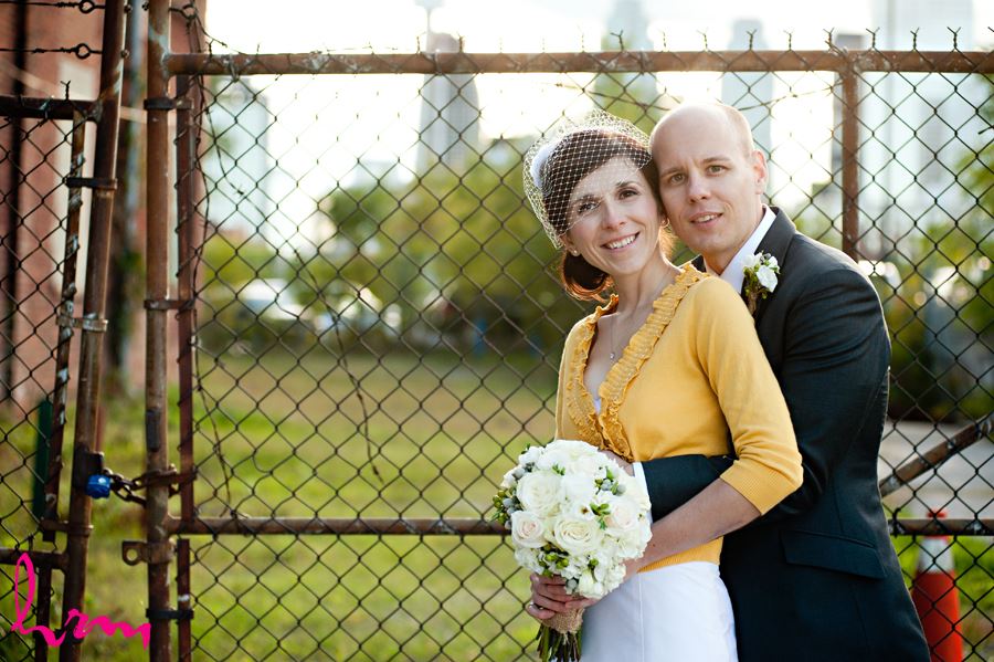 bride and groom in front of fence smiling