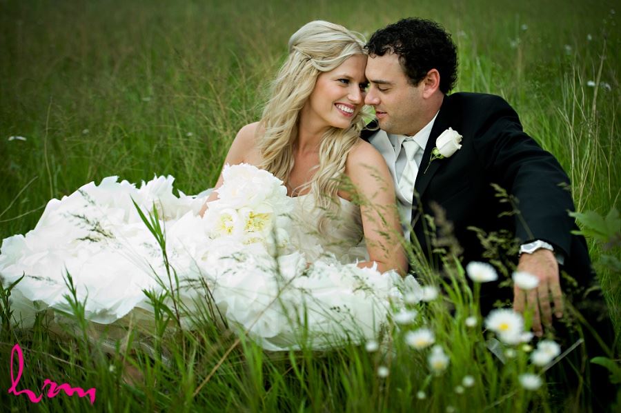 Wedding photo of bride and groom sitting in grass