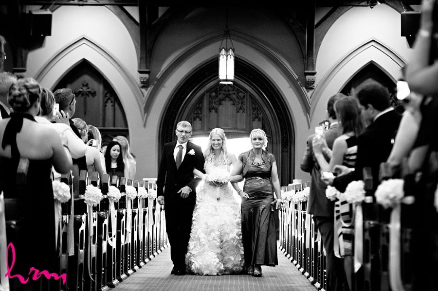 black and white wedding photo of bride walking down aisle with parents