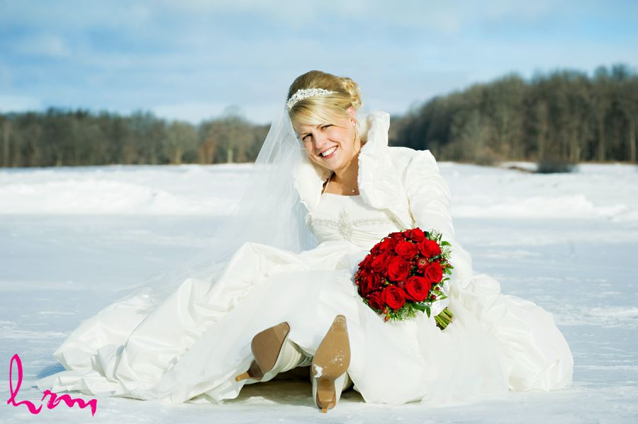 winter bride sitting in the snow with red roses
