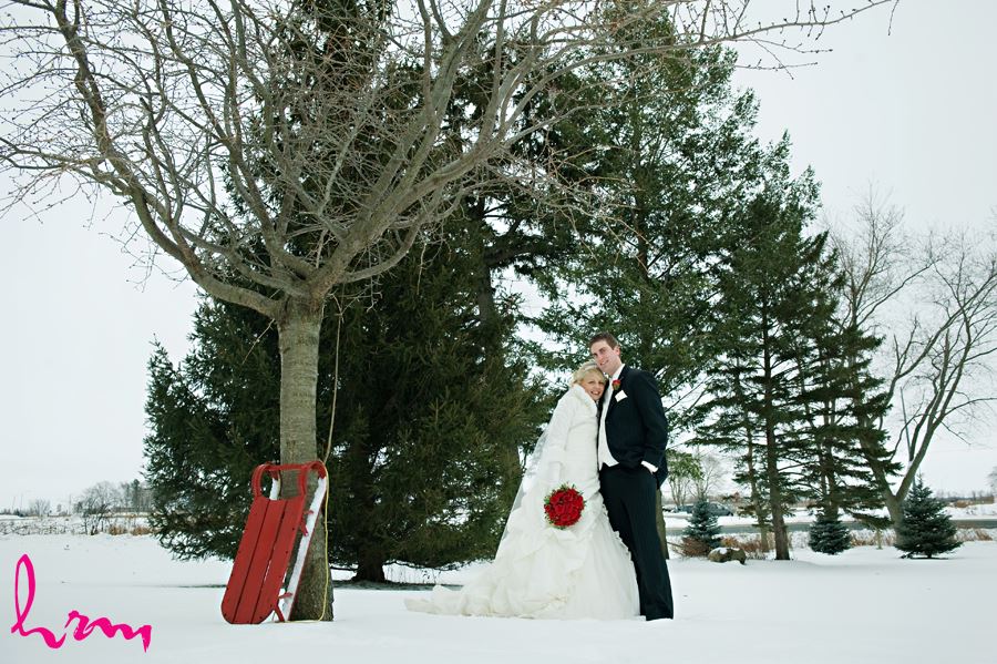 bride and groom by a tree in the snow with a sled