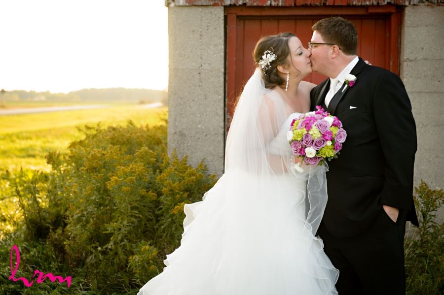 bride and groom kissing in field with barn