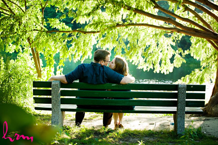 Engaged couple cuddling on a bench near the lake