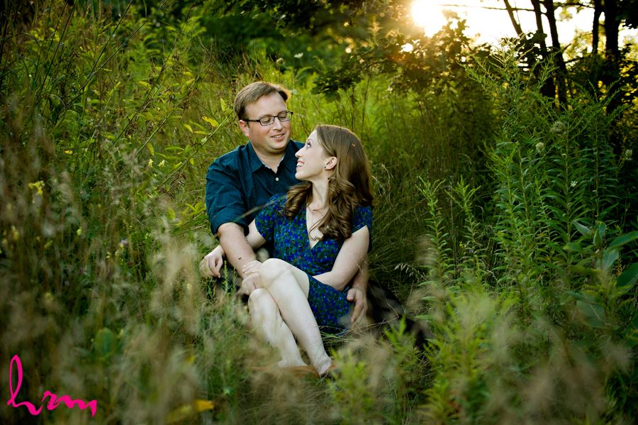 Engaged couple cuddling in grass at sunset