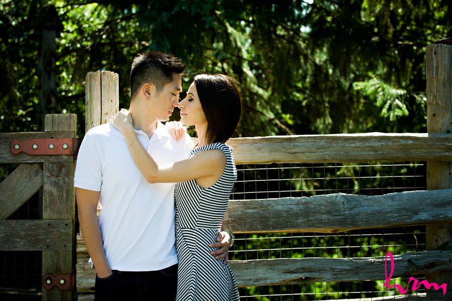 Engaged couple snuggling in front of wooden fence