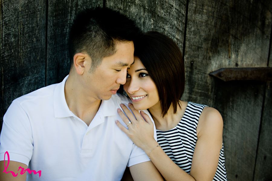 Engaged couple cuddling in front of wooden structure