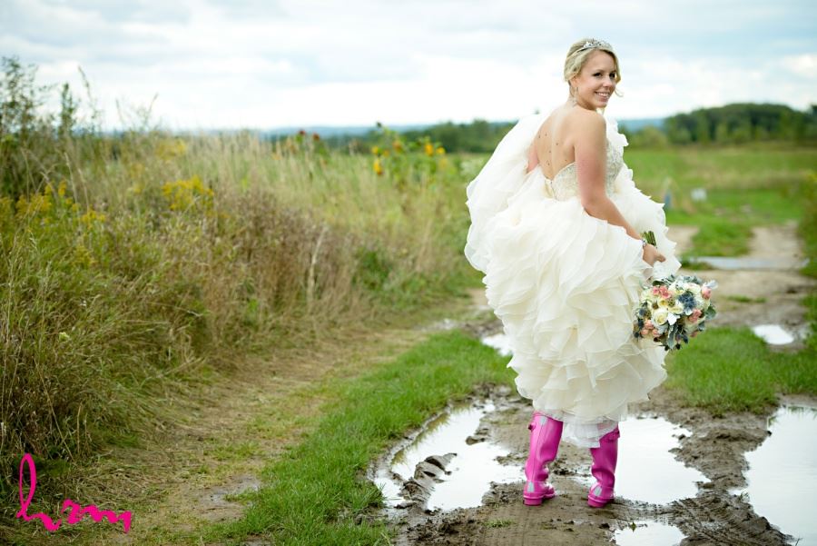 Bride in hot pink galloshes rain boots in puddle on wedding day