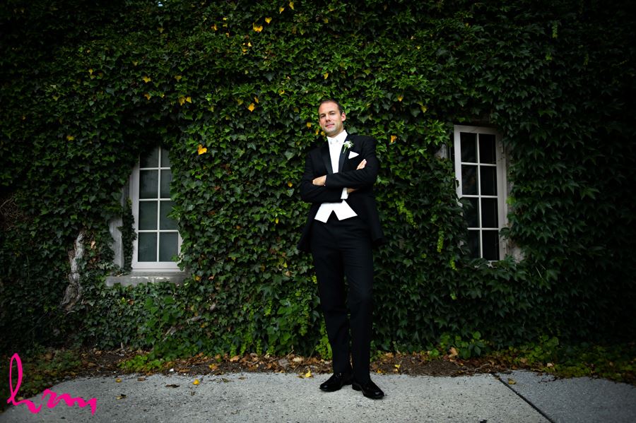 Groom standing in front of wall filled with green leaves at Western University